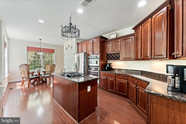 kitchen with dark wood-style floors, stainless steel appliances, a notable chandelier, a center island, and visible vents