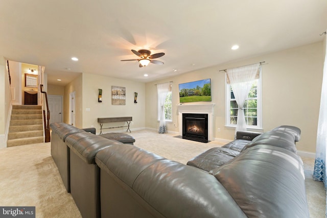 living area featuring light colored carpet, baseboards, a ceiling fan, and stairs