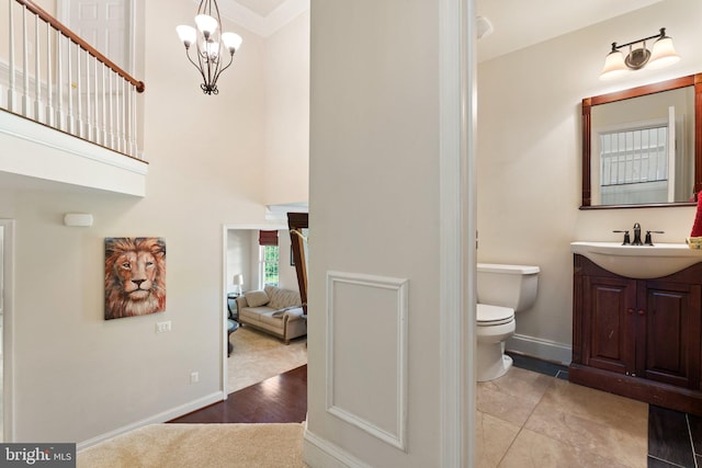 bathroom with a high ceiling, vanity, a notable chandelier, toilet, and baseboards