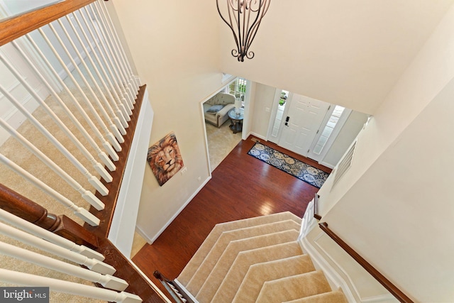 entrance foyer with a chandelier, baseboards, a towering ceiling, wood finished floors, and stairs