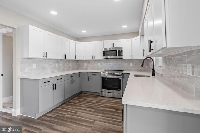 kitchen with light stone countertops, dark wood finished floors, a sink, stainless steel appliances, and backsplash