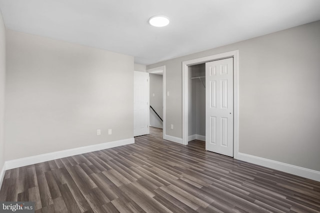 unfurnished bedroom with a closet, dark wood-type flooring, and baseboards