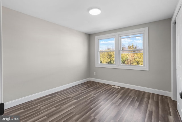 spare room with baseboards and dark wood-type flooring