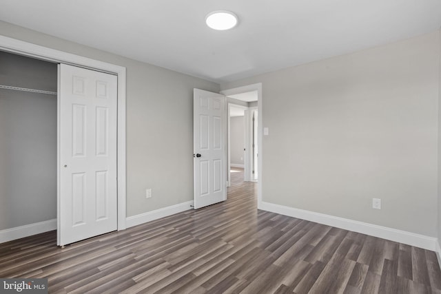 unfurnished bedroom with dark wood-style floors, baseboards, and a closet