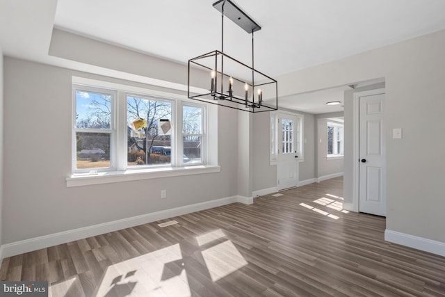 unfurnished dining area featuring baseboards, plenty of natural light, a chandelier, and dark wood finished floors
