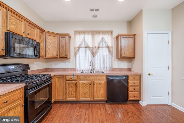 kitchen featuring light wood finished floors, a sink, visible vents, light countertops, and black appliances