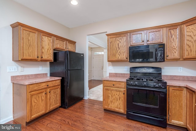 kitchen featuring baseboards, recessed lighting, wood finished floors, light countertops, and black appliances