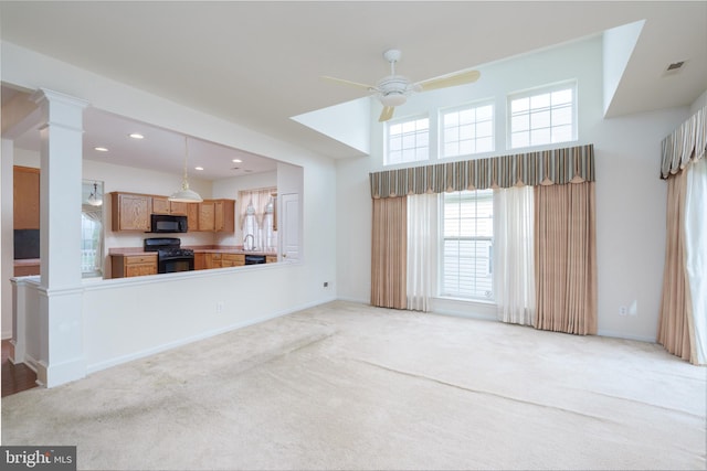 unfurnished living room with a ceiling fan, light colored carpet, baseboards, visible vents, and ornate columns