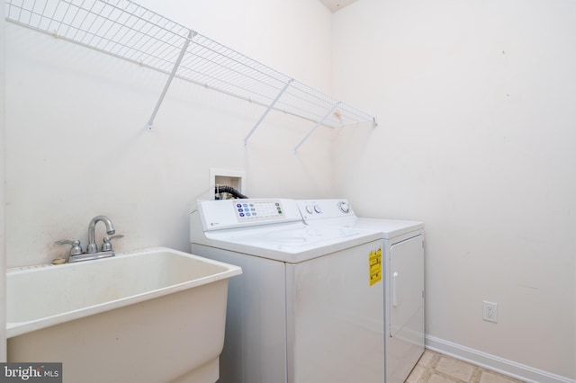 clothes washing area with washing machine and clothes dryer, a sink, laundry area, and baseboards
