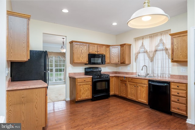kitchen featuring light countertops, a sink, decorative light fixtures, black appliances, and dark wood-style flooring