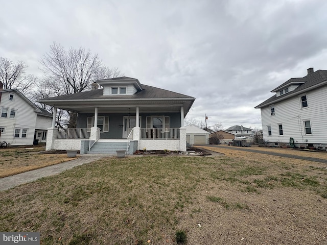 bungalow-style home with a garage, covered porch, an outdoor structure, and a front lawn