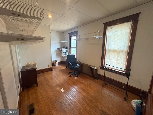 unfurnished office with hardwood / wood-style floors, radiator, visible vents, baseboards, and a paneled ceiling