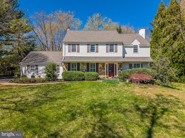 traditional-style house with a front lawn, a shingled roof, stone siding, and a chimney