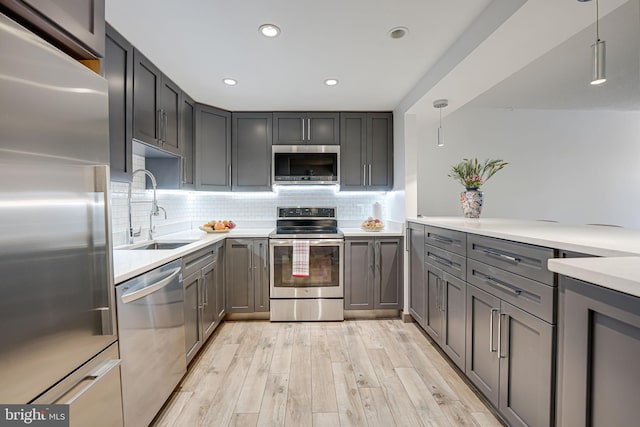 kitchen featuring light wood finished floors, gray cabinets, a sink, appliances with stainless steel finishes, and tasteful backsplash