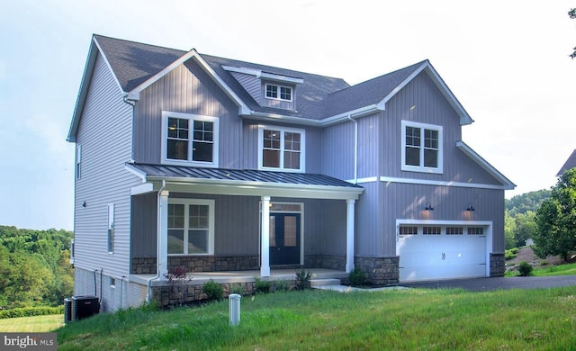 view of front of house with a front yard, cooling unit, covered porch, a garage, and stone siding