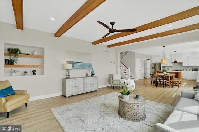 living room featuring visible vents, beam ceiling, light wood-style flooring, a ceiling fan, and stairs
