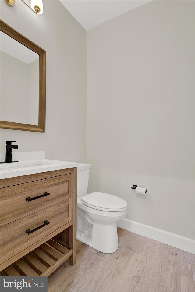 half bath with vanity, toilet, wood finished floors, and baseboards