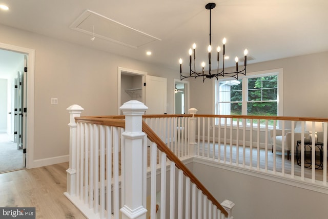 corridor with an upstairs landing, attic access, baseboards, and wood finished floors