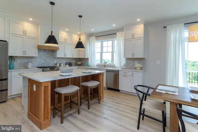 kitchen featuring a sink, a kitchen breakfast bar, a center island, appliances with stainless steel finishes, and light wood finished floors