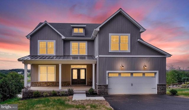 view of front facade with an attached garage, covered porch, french doors, stone siding, and aphalt driveway