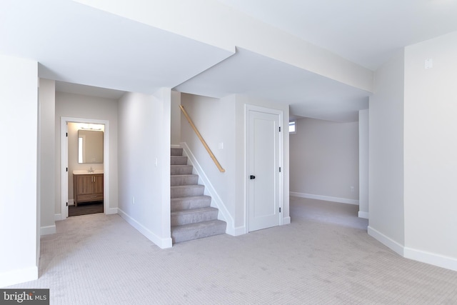 finished below grade area featuring stairs, baseboards, carpet floors, and a sink