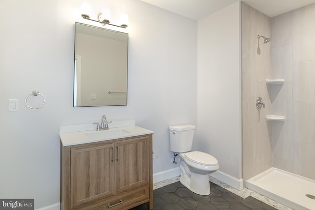 full bath with vanity, baseboards, tiled shower, tile patterned flooring, and toilet