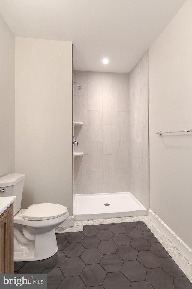 bathroom featuring tiled shower, toilet, vanity, and baseboards