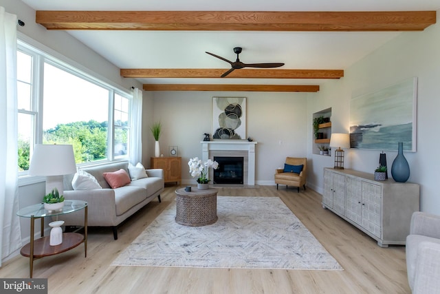 living room featuring a fireplace with flush hearth, beam ceiling, a ceiling fan, light wood finished floors, and baseboards