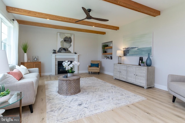 living room featuring ceiling fan, baseboards, beam ceiling, wood finished floors, and a glass covered fireplace