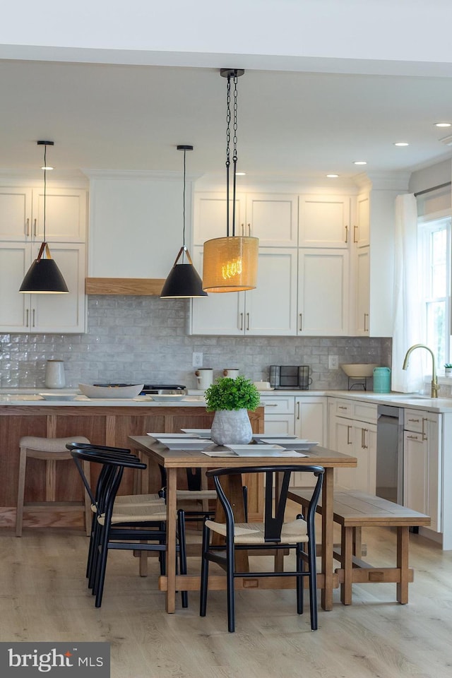 kitchen with pendant lighting, a sink, backsplash, white cabinetry, and light countertops