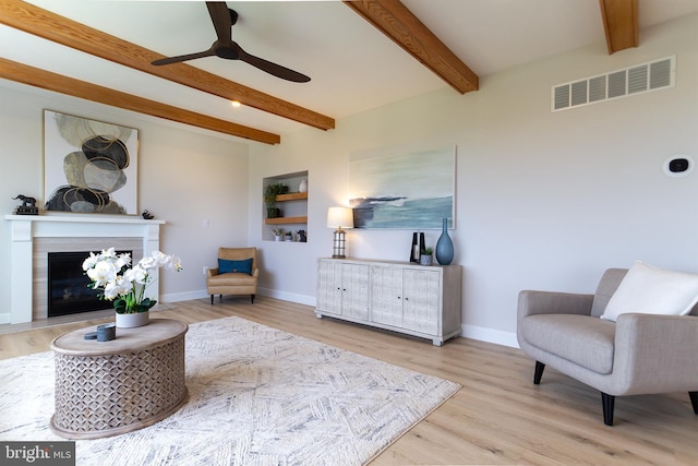 living area featuring wood finished floors, a ceiling fan, visible vents, baseboards, and beamed ceiling