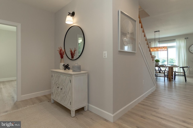 hall featuring light wood-style flooring, baseboards, and a chandelier
