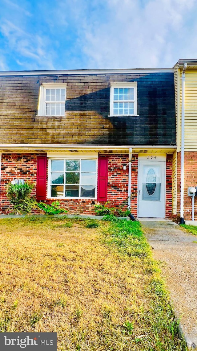 multi unit property featuring brick siding, mansard roof, and a front lawn