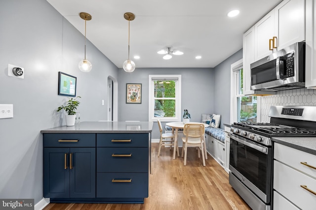 kitchen with a peninsula, white cabinets, appliances with stainless steel finishes, blue cabinets, and light wood-type flooring