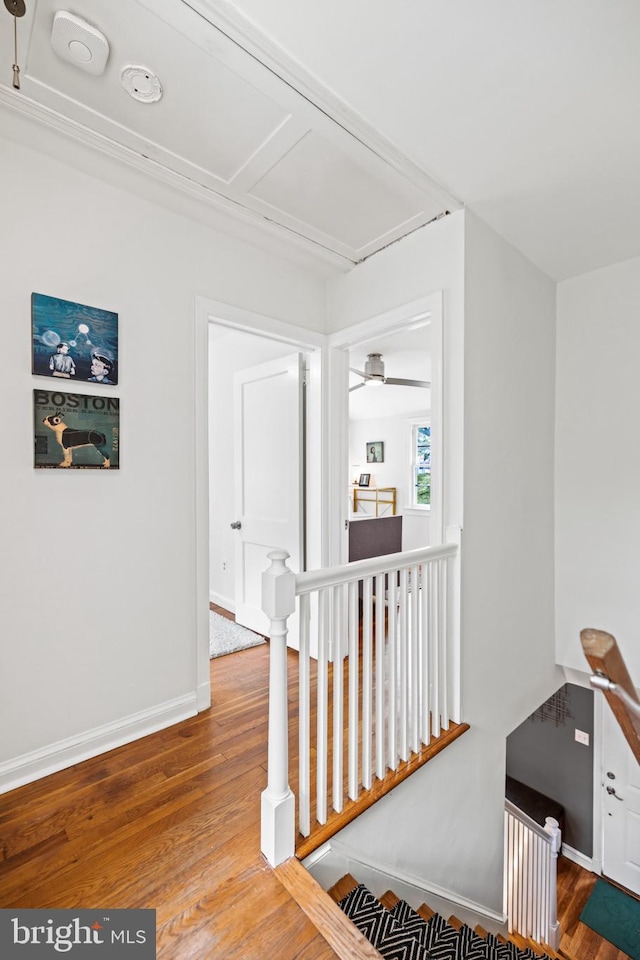 corridor featuring wood finished floors, an upstairs landing, and baseboards
