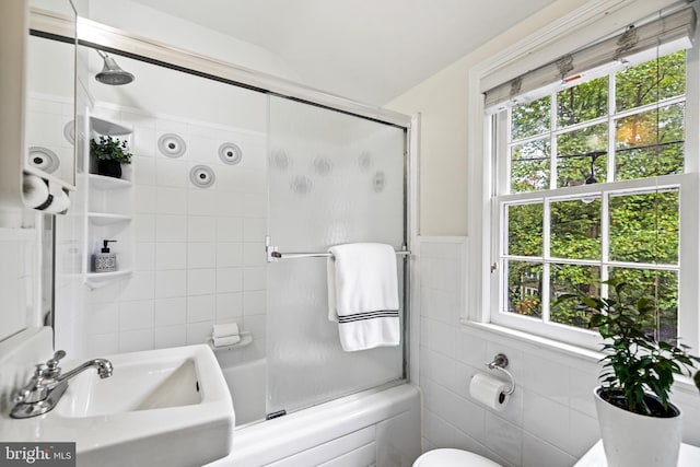 full bath featuring tile walls, toilet, combined bath / shower with glass door, and a sink