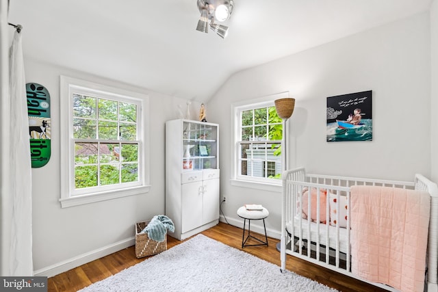 bedroom with vaulted ceiling, baseboards, a nursery area, and wood finished floors