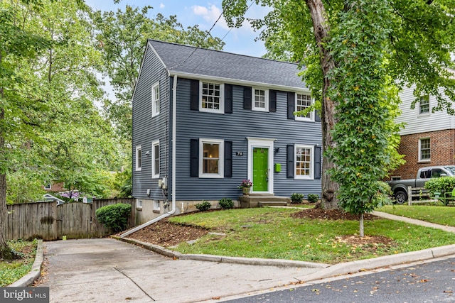 view of front of house with a front yard, fence, driveway, and a shingled roof