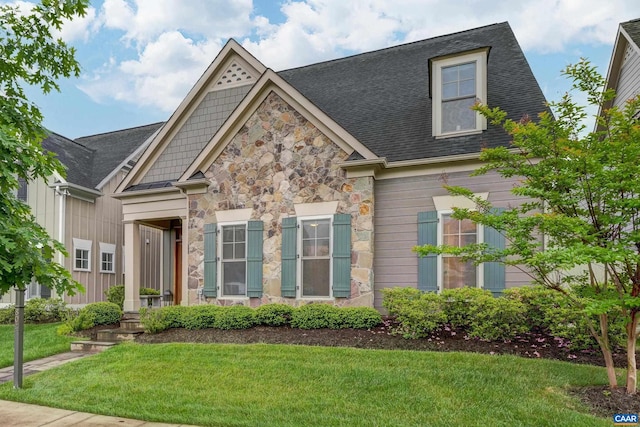 view of front facade featuring stone siding, a shingled roof, and a front yard