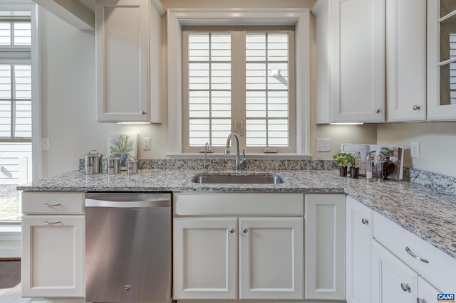 kitchen featuring stainless steel dishwasher, light stone countertops, white cabinetry, and a sink