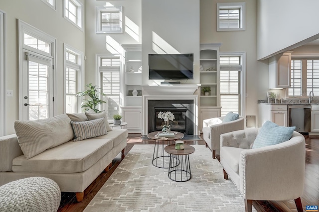 living area with a fireplace with flush hearth, wood finished floors, and a towering ceiling