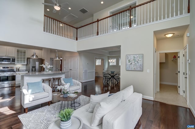 living room with visible vents, dark wood-type flooring, a ceiling fan, baseboards, and a towering ceiling