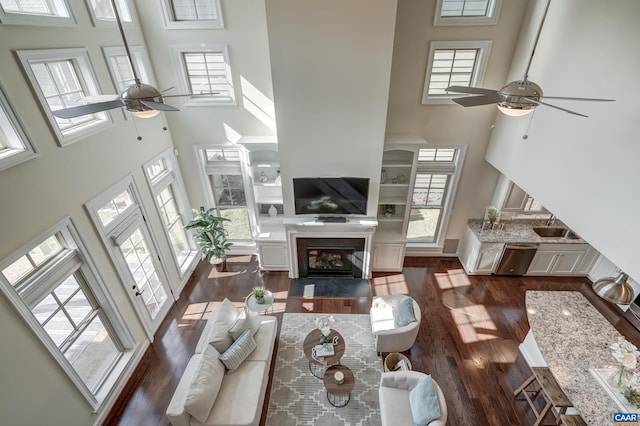 living area with dark wood finished floors, a fireplace with flush hearth, a high ceiling, and a ceiling fan