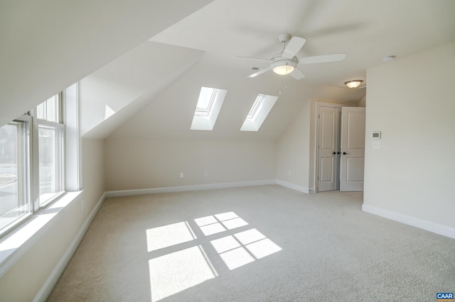 bonus room featuring lofted ceiling with skylight, light colored carpet, a healthy amount of sunlight, and a ceiling fan