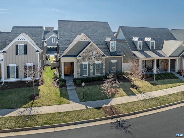 view of front facade featuring stone siding, a shingled roof, a front lawn, and fence