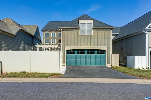 view of front facade with fence, roof with shingles, an attached garage, aphalt driveway, and board and batten siding