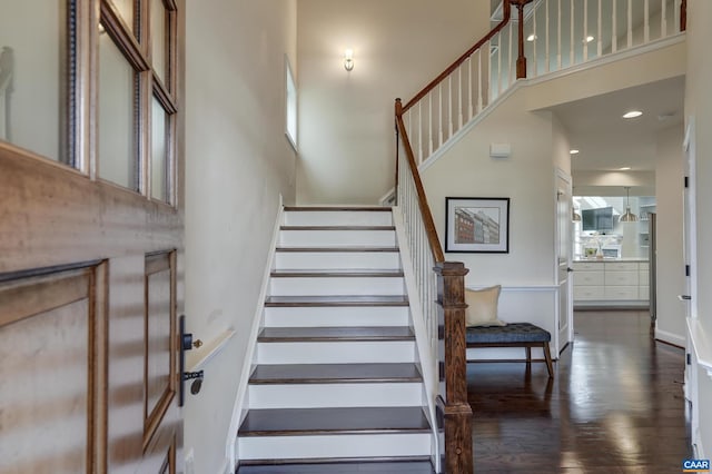 stairway featuring recessed lighting, a towering ceiling, and wood finished floors