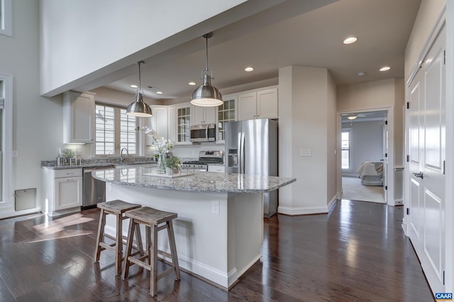 kitchen featuring a breakfast bar, white cabinetry, appliances with stainless steel finishes, glass insert cabinets, and dark wood-style flooring