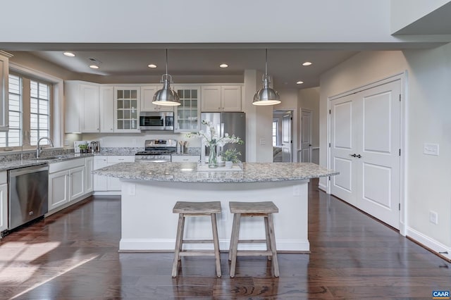 kitchen with a center island, dark wood-type flooring, stainless steel appliances, white cabinetry, and a sink