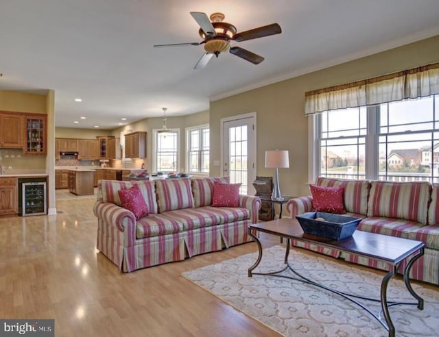 living room featuring light wood-style floors, a ceiling fan, ornamental molding, and wine cooler